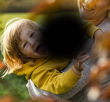 An image of a woman lifting a smiling child. The image has a black blob in the centre with blurred edges, obscuring the centre of the image.