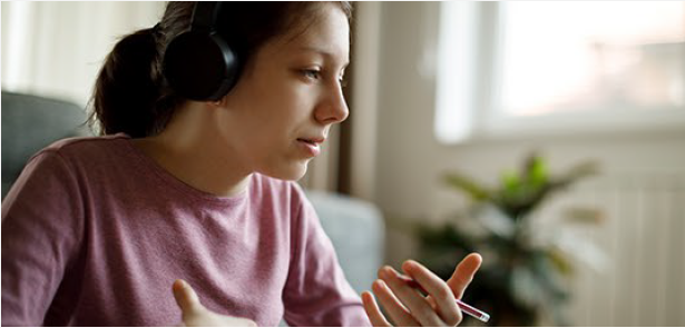 Image of a woman wearing headphones and speaking, gesticulating with her hands and holding a pencil.